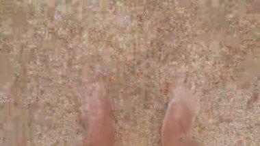 Su insanın ayaklarını yıkar. Deniz dalgalarında erkek ayakları. Ayaklar deniz suyunda, yakın plan.