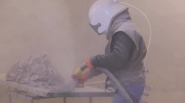 Kum patlaması metal parçaları. Adam ayrıntıları zımparalıyor. Kumlama silahı.