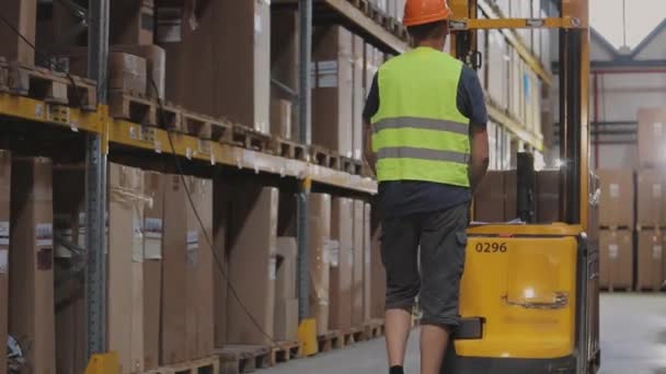 Ein Arbeiter mit einem elektrischen hydraulischen Gabelstapler mit Waren. Arbeiter Gabelstapler im Lager. Der Arbeiter geht durch das Lager — Stockvideo