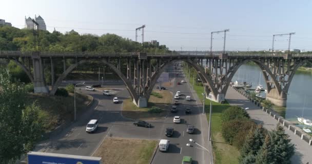 Samochody jadą wzdłuż drogi w mieście widok z góry. Samochody przejeżdżają pod mostem. Wiele samochodów na drodze przejeżdżających pod mostem widok z góry. Ruch samochodowy. — Wideo stockowe