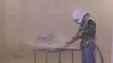Adam ayrıntıları zımparalıyor. Kum patlaması metal parçaları. Kumlama silahı.