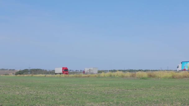 Ciężarówka z czerwoną kabiną jedzie wzdłuż autostrady. Ciężarówka jedzie wzdłuż drogi. Dostawa towarów ciężarówką — Wideo stockowe