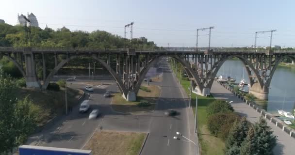 Ruch samochodowy. Samochody jadą wzdłuż drogi w mieście widok z góry. Samochody przejeżdżają pod mostem. Wiele samochodów na drodze przejeżdżających pod mostem widok z góry — Wideo stockowe