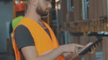 Büyük bir fabrikanın depo müdürü. Bir depoda elinde tablet olan bir müdür malları kontrol ediyor..