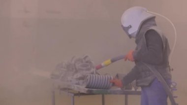 Kum patlaması metal parçaları. Adam ayrıntıları zımparalıyor. Kumlama silahı.