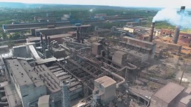 Dumanı tüten bacası olan büyük bir metal bitkinin üzerinden uçmak. Fabrikanın bacasından duman salınımı. Fabrika insansız hava aracı görüntüsünün bacasından yoğun duman çıkıyor.