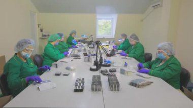 Maskeli işçiler. Fabrika işçileri ilaç şişliklerini kutulara doldurur. Fabrikada ilaç ambalajı.