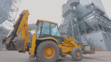 Sarı bir traktör fabrikanın bölgesinden geçiyor. Sarı traktör hareket halinde. Traktör fabrikadan geçiyor.