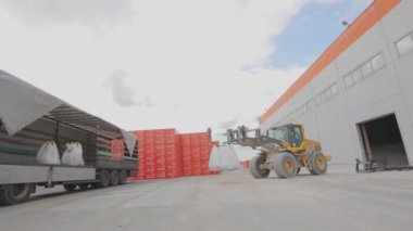 Bir buldozer bir kamyona torba yükler. Malları kamyona yüklüyorum.