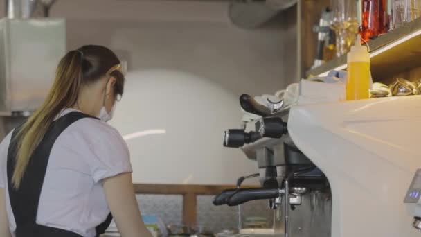 Een gemaskerde barista zet koffie, mensen werken in een masker, werken na quarantaine. Koffie zetten — Stockvideo
