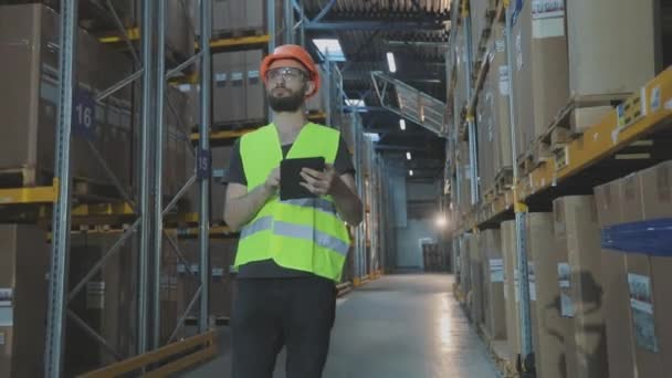 Egy munkás a raktárban megcsinálja a kört. Férfi táblagéppel a gyár raktárában — Stock videók