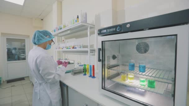 Una mujer en el laboratorio haciendo trabajo. Asistente de laboratorio enmascarado. trabajador de laboratorio. — Vídeo de stock