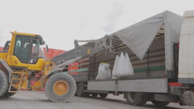 Bir buldozer çantaları bir kamyona boşaltır. Malları kamyondan boşaltıyorum. Buldozer arabadan mal indirir.