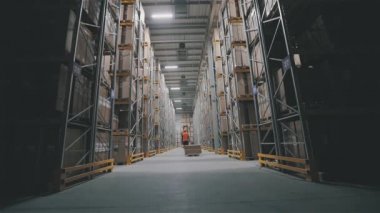Turuncu yelekli bir adam depoda kutu taşıyor. Fabrikada iş gününün sonunda. Depodaki ışıkları kapatıyorum.