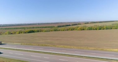 Bir kargo kamyonu otoyol boyunca gidiyor. İnsansız hava aracı görüntüsü. Vagon, tarlaların üst manzarası arasında virajlı bir yolda ilerliyor.