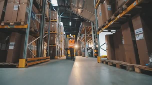 Рабочий перевозит груз через склад. Рабочий проходит через склад с электрическим гидравлическим погрузчиком. — стоковое видео