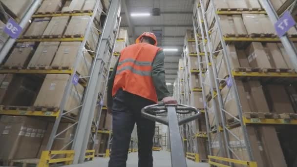 オレンジのベストの男が倉庫にパレットトラックを運ぶ — ストック動画