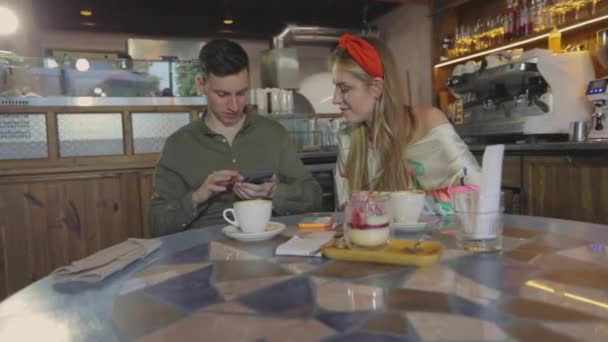 レストランで男の隣の女の子がコーヒーを飲む。男と女が電話を見てカップルがスマートフォンで写真を見せる. — ストック動画