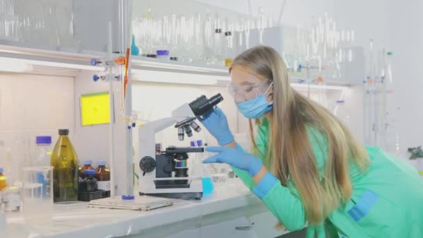 Het uitvinden van een vaccin tegen het coronavirus. jong meisje viroloog kijkt door een microscoop — Stockvideo