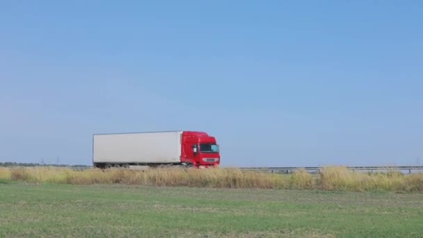 Egy fehér kocsi halad végig az autópályán napsütéses időben. Teherautó az autópályán — Stock videók