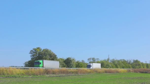 Twee vrachtwagens rijden langs de weg naast elkaar. Vrachtwagens rijden langs de snelweg — Stockvideo