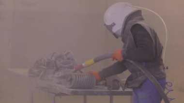 Adam ayrıntıları zımparalıyor. Kum patlaması metal parçaları. Kumlama silahı.