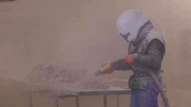 Kum patlaması metal parçaları. Adam ayrıntıları zımparalıyor. Kumlama silahı.