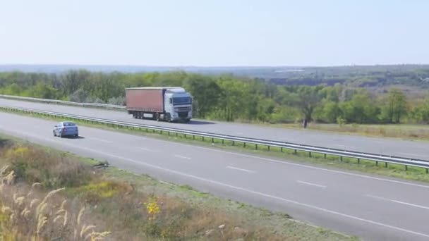 빨간 트레일러가 있는 트럭 이 고속도로를 따라 달리고 있습니다. 트럭 이 도로를 따라 달리고 있어요. 트럭으로 물건을 배달하는 모습 — 비디오