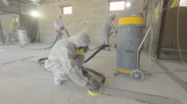 Koruyucu giysiler içindeki işçiler beton zemini öğütüyor. İnşaat alanında çalışma süreci. İnşaat işçileri. İşçiler beton döşeme yapıyor