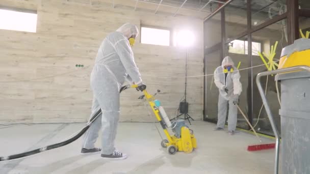 Werknemers in beschermende pakken slijpen de betonnen vloer. Werkproces op een bouwplaats. Bouwvakkers. Werknemers maken betonnen vloer — Stockvideo