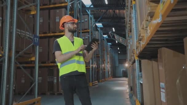 Ένας εργάτης σε μια αποθήκη κάνει ένα γύρο. Άντρας με tablet σε αποθήκη εργοστασίου — Αρχείο Βίντεο