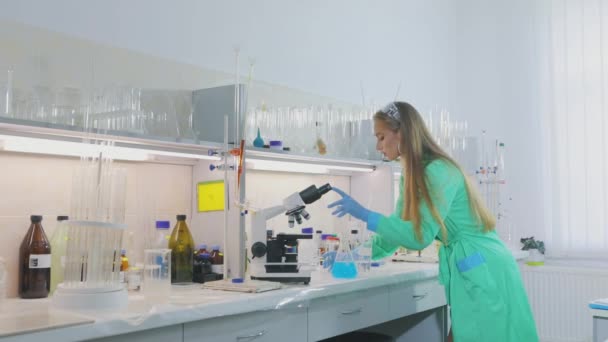 Una hermosa chica en el laboratorio lleva a cabo experimentos. Asistente de laboratorio joven en un laboratorio químico — Vídeo de stock