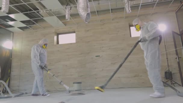 Werknemers in beschermende pakken slijpen de betonnen vloer. Werkproces op een bouwplaats. Bouwvakkers. Werknemers maken betonnen vloer — Stockvideo