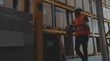 Bir işçi hidrolik forklift ile ağır çekimde yük taşır. Büyük, modern bir depo. Stokta modern özel ekipman