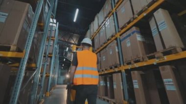Bir işçi elektrikli forkliftle depoya doğru yürür. Bir işçi depodan kargo taşıyor.