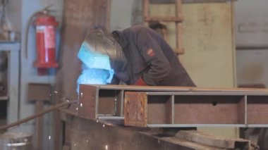 . Kaynakçı fabrikada çalışıyor. Kaynakçı metal bir parça metal kaynak makinesi topluyor.