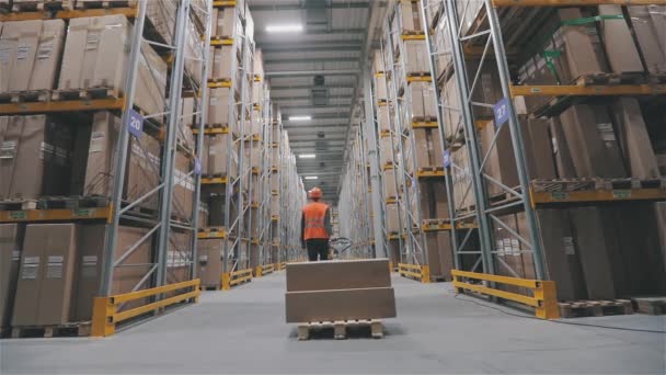 Un hombre con un chaleco naranja lleva cajas en un almacén. Fin de la jornada laboral en la fábrica. Apagando las luces del almacén — Vídeo de stock