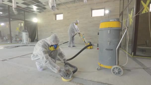 Workers in protective suits are grinding the concrete floor. Working process at a construction site. Construction professionals. Workers make concrete floor — Stock Video