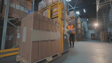 Depoda forklift kullanan bir işçi. İşçi depoya doğru yürür. Depoda çalışan bir işçi elektrikli forklift taşır.