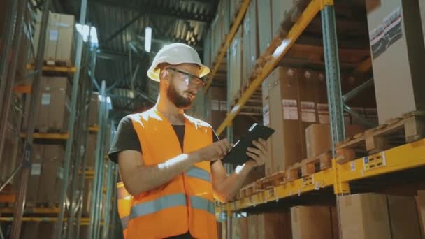 Il direttore del magazzino ispeziona il magazzino. Un uomo in un magazzino moderno. Lavoratore in un casco in un magazzino — Video Stock