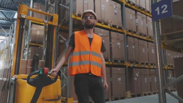 Un trabajador transporta una carga en una carretilla elevadora hidráulica eléctrica. Gran almacén moderno. Equipamiento especial moderno en stock — Vídeo de stock