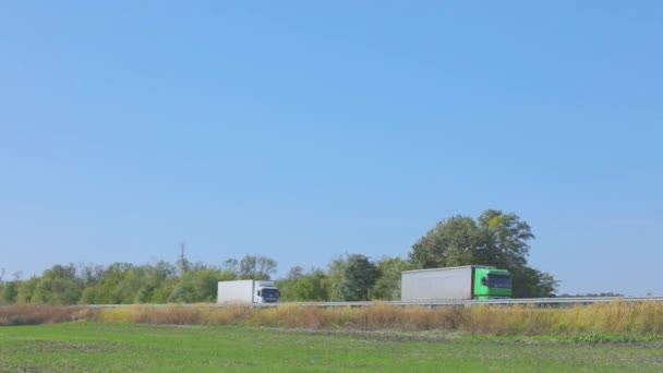 Twee vrachtwagens rijden langs de weg naast elkaar. Vrachtwagens rijden langs de snelweg — Stockvideo
