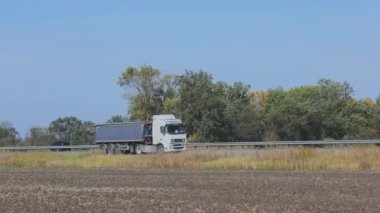 Mavi römorklu bir çöp kamyonu otoyol boyunca gidiyor. Güneşli bir havada uzun bir yolda giden bir kargo kamyonu.