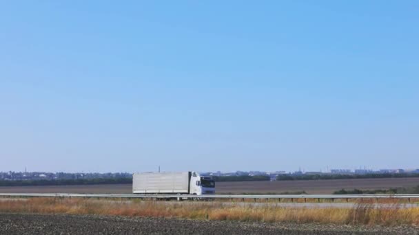 En vit vagn kör längs motorvägen i soligt väder. Lastbil på motorvägen — Stockvideo