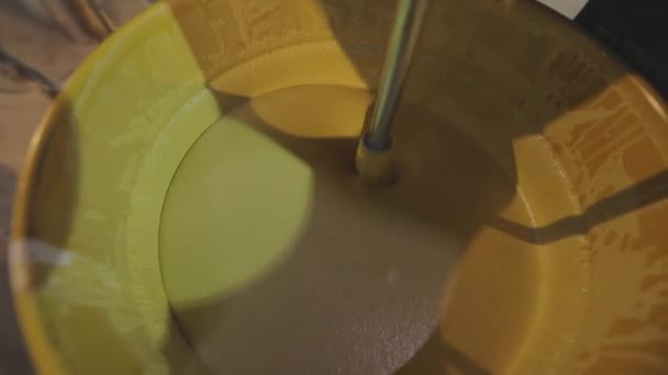 Een close-up van gele verf die in een emmer wordt geroerd. Roeren van verf in een emmer. — Stockvideo