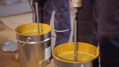 Kovada boya karıştırmak. Yakın plan sarı boya kovada karıştırılıyor.