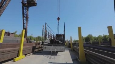 İşçiler bir kamyona metal yükler, insanlar depoda çalışır, kargoyu kamyona yüklerler. Kamyon vincin altında.