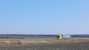 Kamyon otoyolda gidiyor. Kamyon tarlaların ve ağaçların etrafındaki otoyolda ilerliyor.