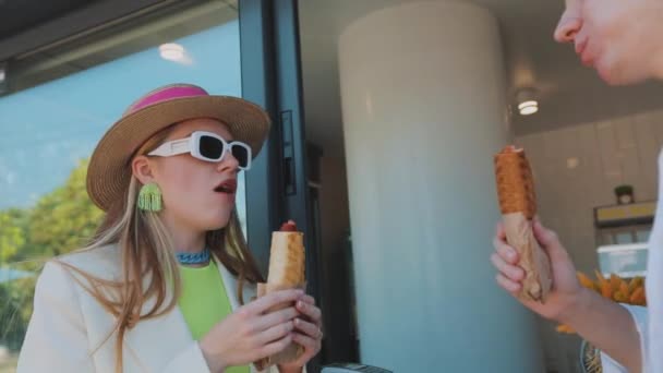 Dziewczyna z facetem jedzącym hot dogi. Stylowa młoda para jedząca hot dogi — Wideo stockowe