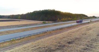 Kamyonlar günbatımı manzaralı düz bir yolda ilerler. Kamyonlar gün batımında otoban boyunca tarlaların arasında gidiyor..
